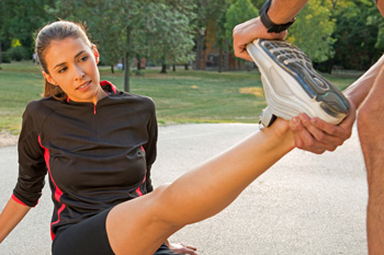 Jogger having leg stretched out at park by friend