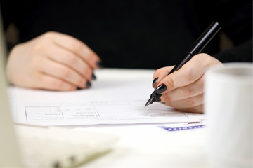 A woman with black nail paint writes on a form with a fountain pen.