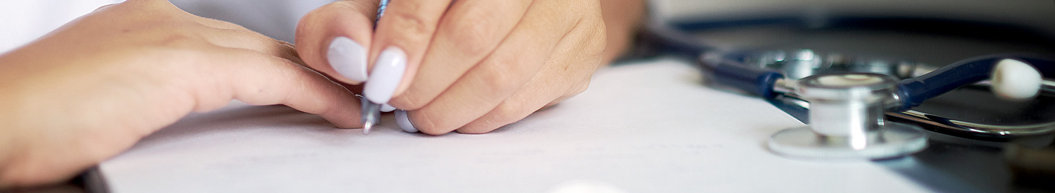 Person filling out paper form with stethoscope on table