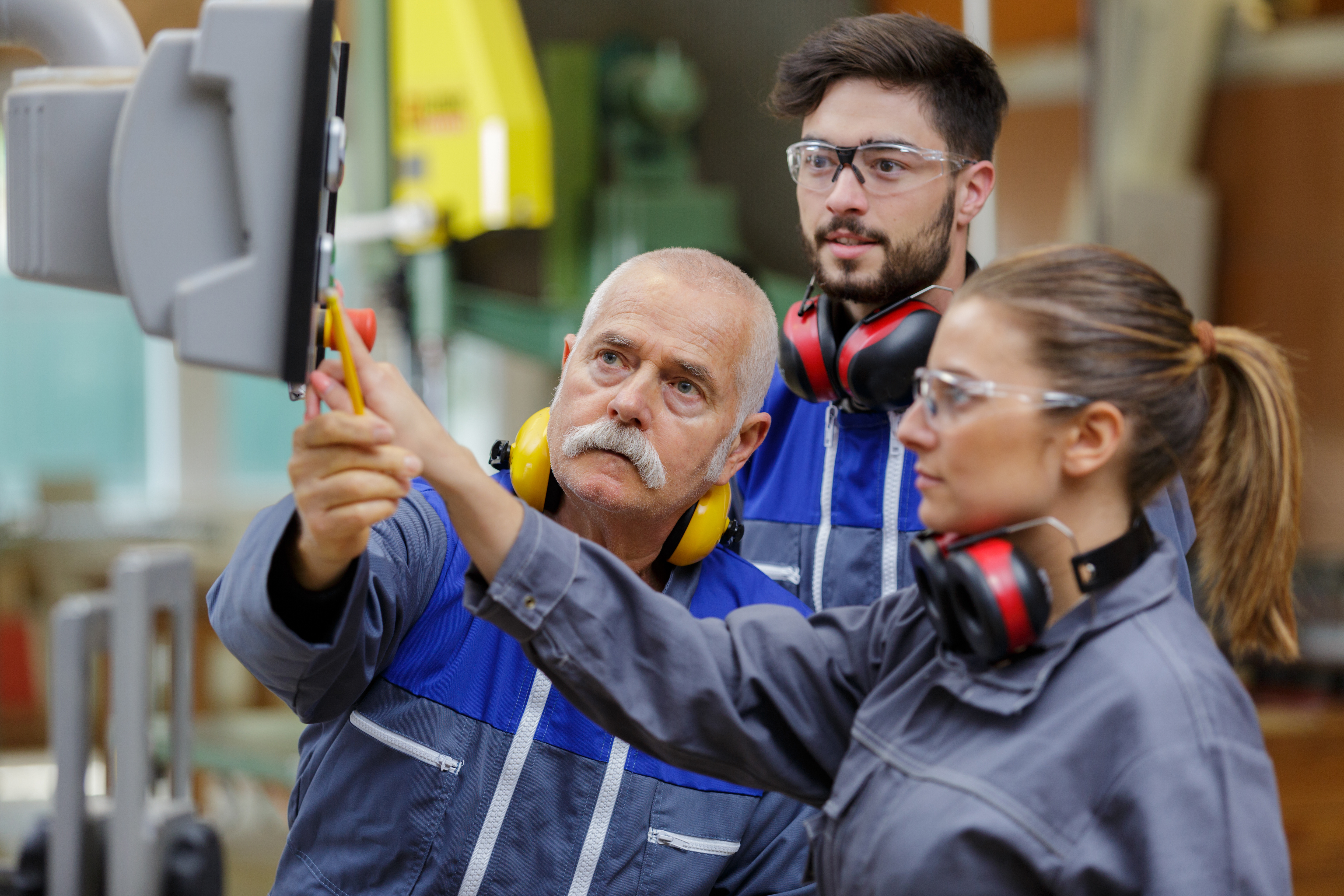 Older male employee explaining machines to two young interns 