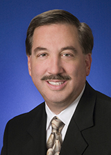 <img alt="A photo of IURC Commissioner David Ziegner, dressed in a black suit, standing against a blue background." />