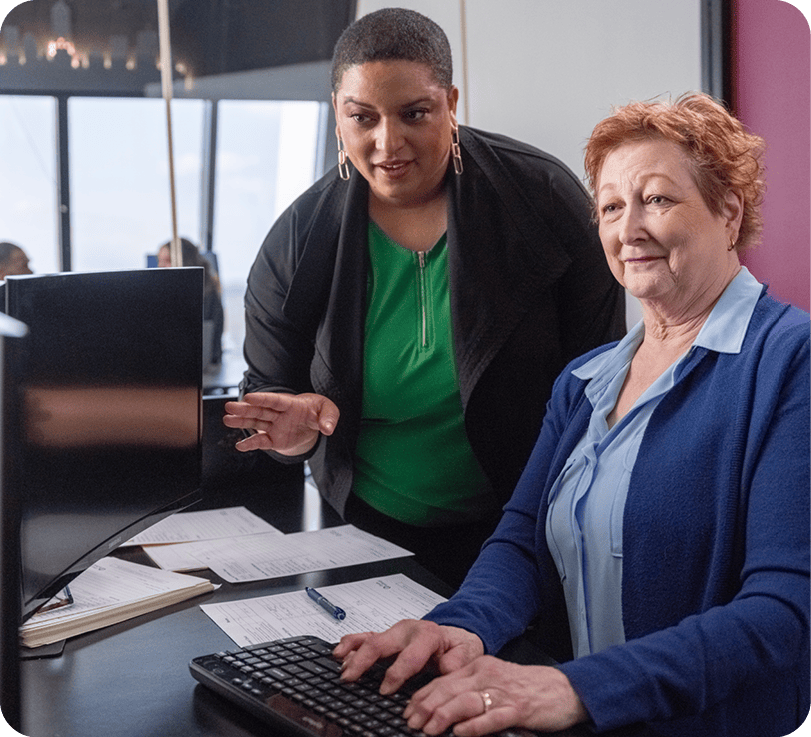 Woman helping older woman at a computer.
