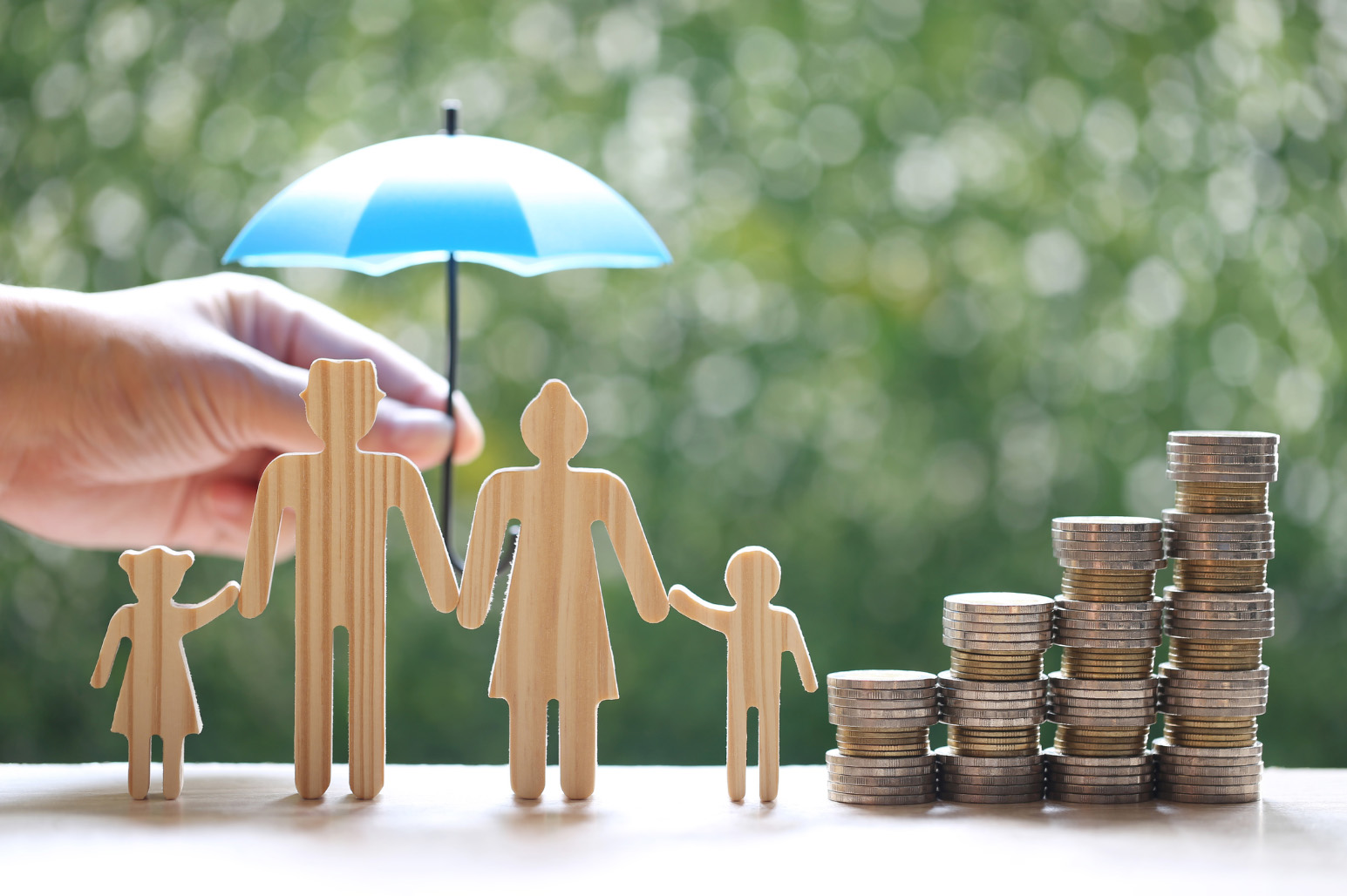 An image of a family made out of wood holding hands next to a pile of coins with an umbrella over them.