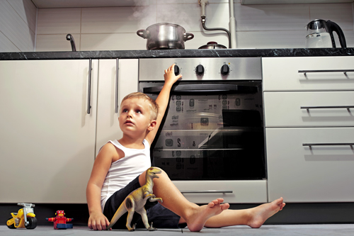 Child turning knob on oven while food steams on stovetop