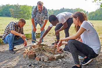 Group of people placing sticks inside campfire ring