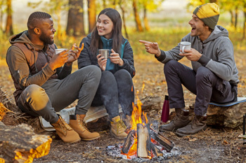 Group of people talking and drinking beverages next to a burning campfire