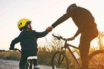Child and parent riding bikes with helmets on fist-bump