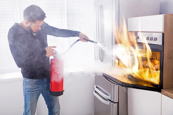 Man using fire extinguisher on flaming oven