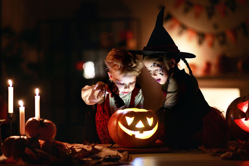 Children in costumes shining a flashlight into a jack o' lantern