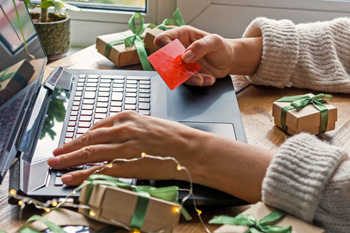 Person at laptop with holiday gift card and boxes