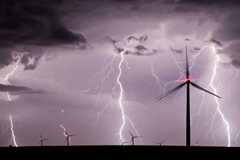 Multiple lightning bolts strike near windmill farm at night