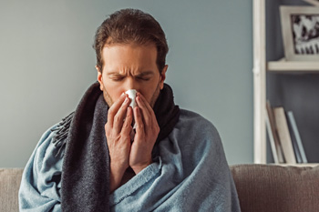 Man blowing nose while covered in scarf and blanket