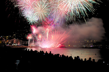 Fireworks over a crowd next to water body