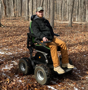 Man in motorized trail chair in woods.
