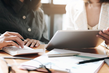 Two people collaborate on taxes. One holds a tablet, and the other holds a calculator.