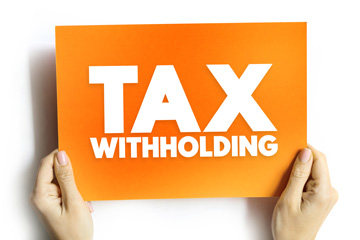 A pair of hands holds a bright orange sign that reads 'Tax Withholding'.