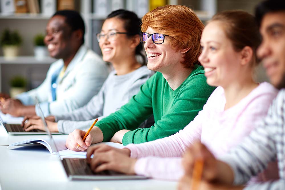 Picture of Engaged Adult Learners Taking Notes in Class and Smiling at Teacher off Camera