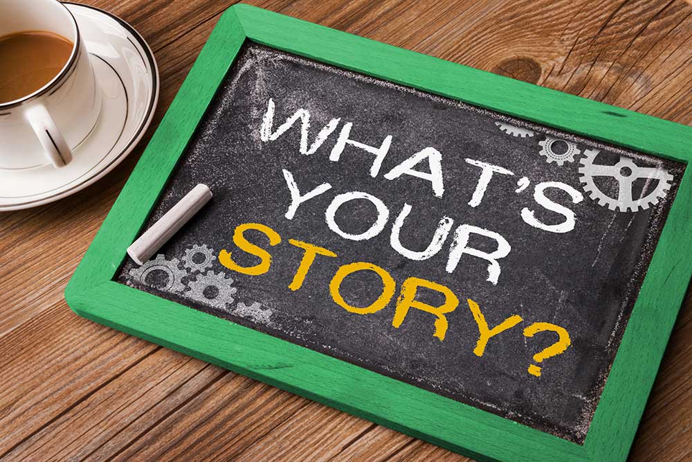 Image of a small chalkboard on a table next to a coffee cup that says, 'What's your Story?"
