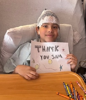 Young boy holds a hand-drawn note that reads, "Thank you, Sam."