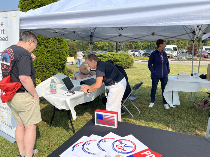 At an outdoor event, a women works at a computer, as a man looks on.