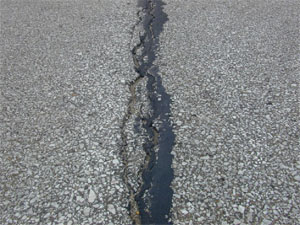 Photo showing a close-up of a wide and severely spalled crack in the asphalt surface.
