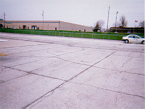 Overview photo of an apron pavement with a uniform rectangular pattern of medium-severity           transverse and longitudinal cracks. The pattern is the result of cracks that have reflected through the asphalt surface at the joints of the PCC slabs below. Some spalling is visible at the cracks.