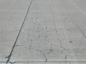 Overview photo of a PCC slab with a noticeable pattern of fine cracks spread over the entire surface area of the slab.           Some of the cracks are spalled.