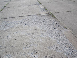 Overview photo showing showing high-severity scaling. The PCC pavement surface in this photo           is severely scaled, and there is noticeable loose material on the surface.
