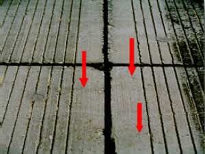 Close-up photo showing multiple small hairline shrinkage cracks on the pavement surface.           Three red arrows are drawn on the photo to point to the location of the visible shrinkage cracks.