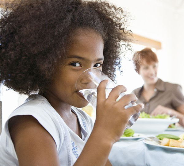 A child drinking a glass of water at the dinner table.