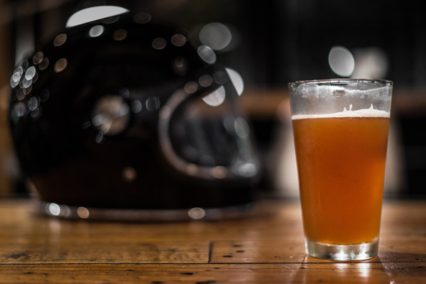 Pint of beer sitting on a table in the foreground with a motorcycle helmet in the background