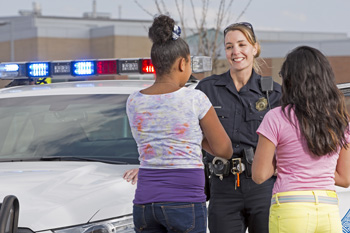 Police officer smiles with children by police car
